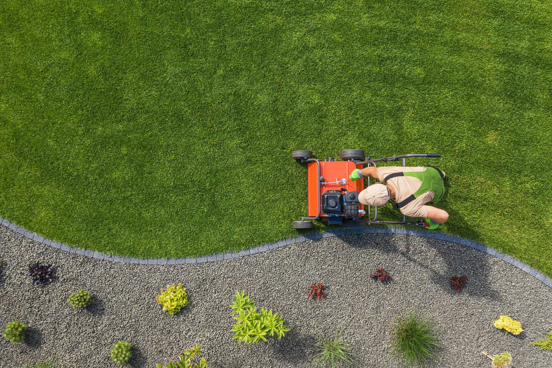 Scène extérieure de jardinage professionnel avec homme utilisant une tondeuse autoportée orange sur pelouse verte entretenue